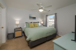 A bedroom with a bed, bedside lamps, a ceiling fan, a window with curtains, and a desk with a television. - Coastal Sage 2bd/2ba Rehoboth/Dewey Beach (Rehoboth Beach)