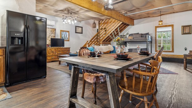 A rustic kitchen with a wooden dining table, chairs, and a black refrigerator. - Davy Jones' Loft, Treehouse, and Treasure Hunt! (Wilmington)