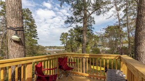 A wooden deck with two red folding chairs and a bench, overlooking a body of water and trees. - Davy Jones' Loft, Treehouse, and Treasure Hunt! (Wilmington)