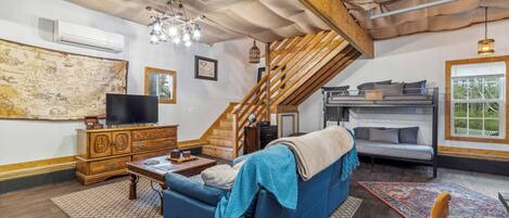Ein gemütliches Wohnzimmer mit einem blauen Sofa, Holzmöbeln, einer Treppe und einem großen Fenster.