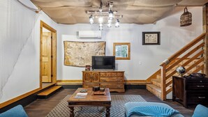 A cozy living room with a wooden staircase, a television, a map on the wall, and a globe on a side table. - Davy Jones' Loft, Treehouse, and Treasure Hunt! (Wilmington)