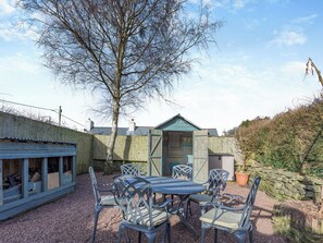 A patio area with a table and chairs, a wooden shed, and a stone wall.