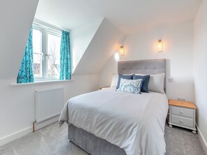 A bedroom with a bed, a nightstand, a window with curtains, and a radiator.