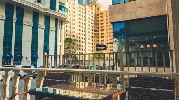 A rooftop terrace with wicker furniture and a glass table, overlooking a cityscape with modern buildings. - Deluxe İnn Hotel Baku (Baku)