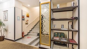 A hotel lobby with a staircase, a fire extinguisher, a potted plant, and a bookshelf. - Deluxe İnn Hotel Baku (Baku)