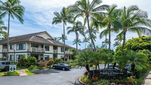 A hotel with a two-story structure, a parking area, and a landscaped garden with palm trees.