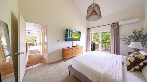 A bedroom with a bed, a TV, a dresser, and a window with a view of greenery.