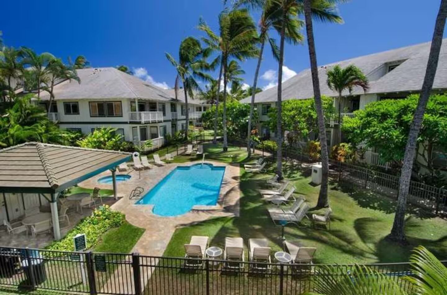 A resort with a swimming pool, lounge chairs, and palm trees.