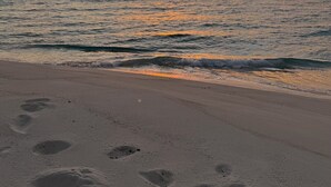 Ein Strand mit Fußspuren, die zum Wasser führen, ein Sonnenuntergang im Hintergrund und eine ruhige See.