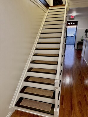 A staircase with white walls and wooden steps, leading to an exit door.