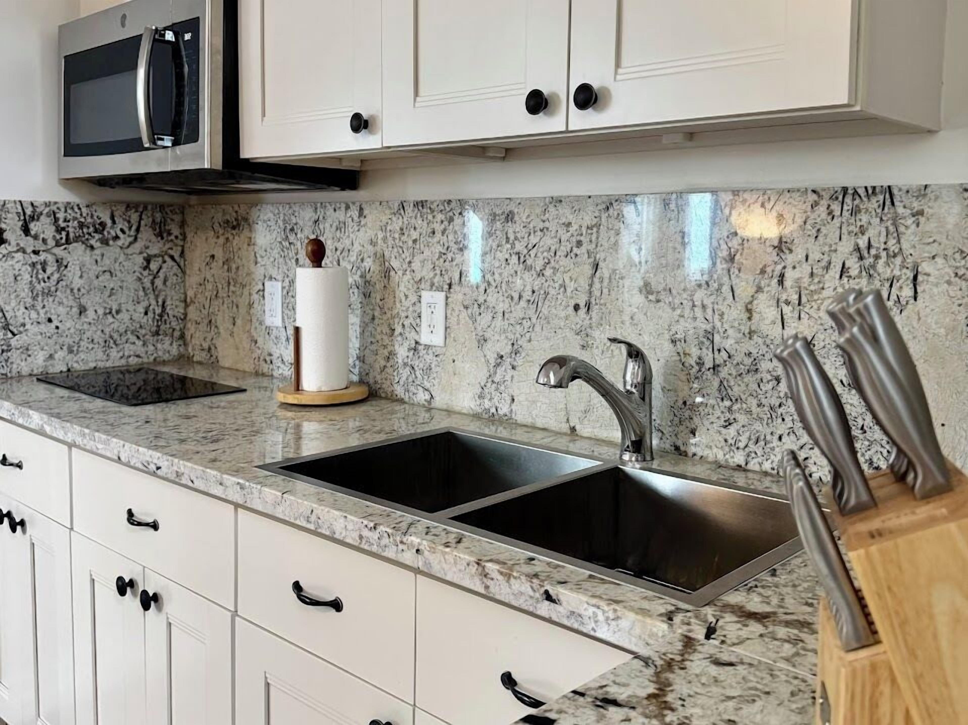 A kitchen with white cabinets, a stainless steel sink, a modern faucet, and a microwave.