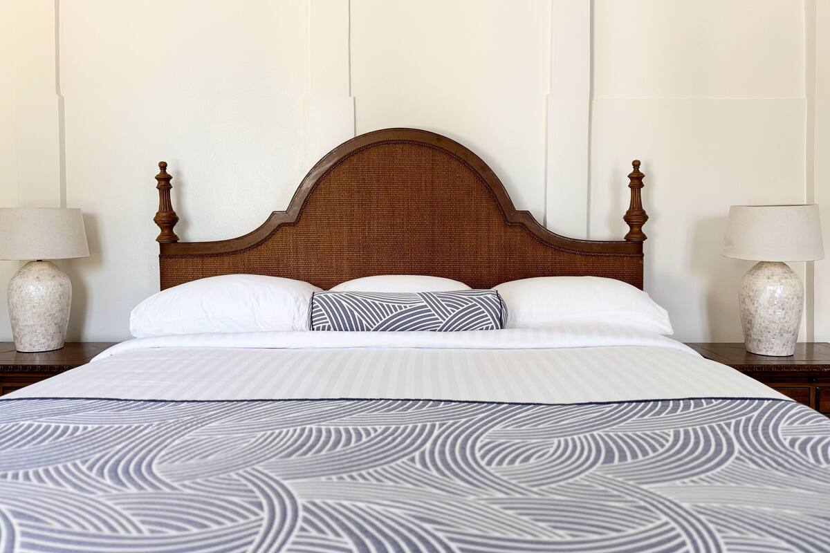 A neatly made bed with a patterned bedspread, a wooden headboard, and two bedside lamps.