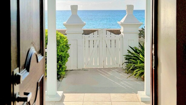Eine offene Tür, die zu einem verschlossenen Weg mit Blick auf das Meer führt.