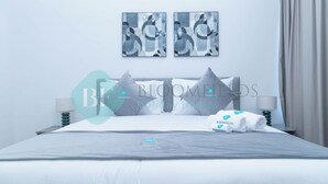 A neatly made bed with a grey blanket, pillows, and a folded towel. There are two wall-mounted artworks above the bed. - Bloomfields 1BR Ocean View in Oceanscape (Abu Dhabi)