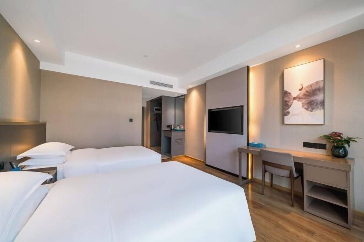 A modern hotel room with two beds, a desk, a chair, a flat-screen TV, and a painting on the wall.