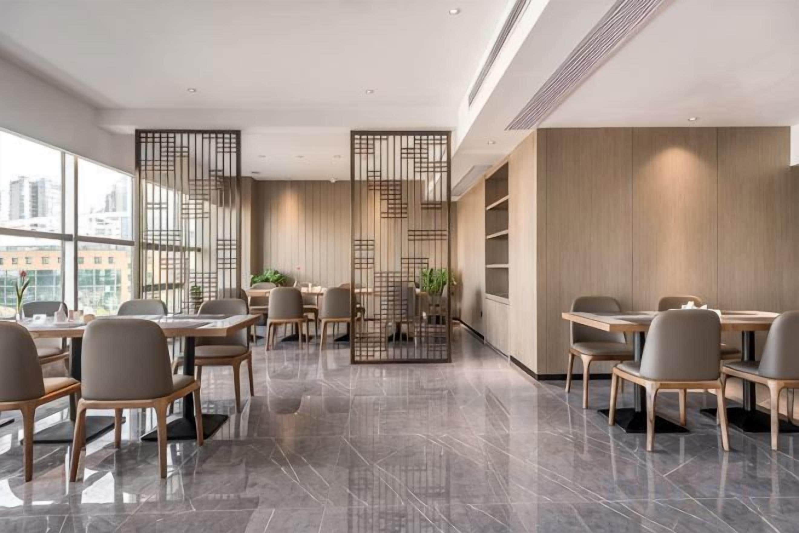A modern dining area with multiple tables and chairs, a decorative partition, and large windows offering a city view.