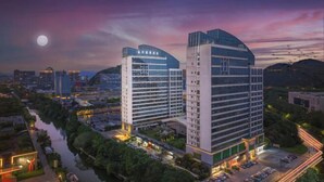 A modern hotel with multiple high-rise buildings, a parking area, and a river in the foreground. - Jade Crystal Hotel (Taizhou)