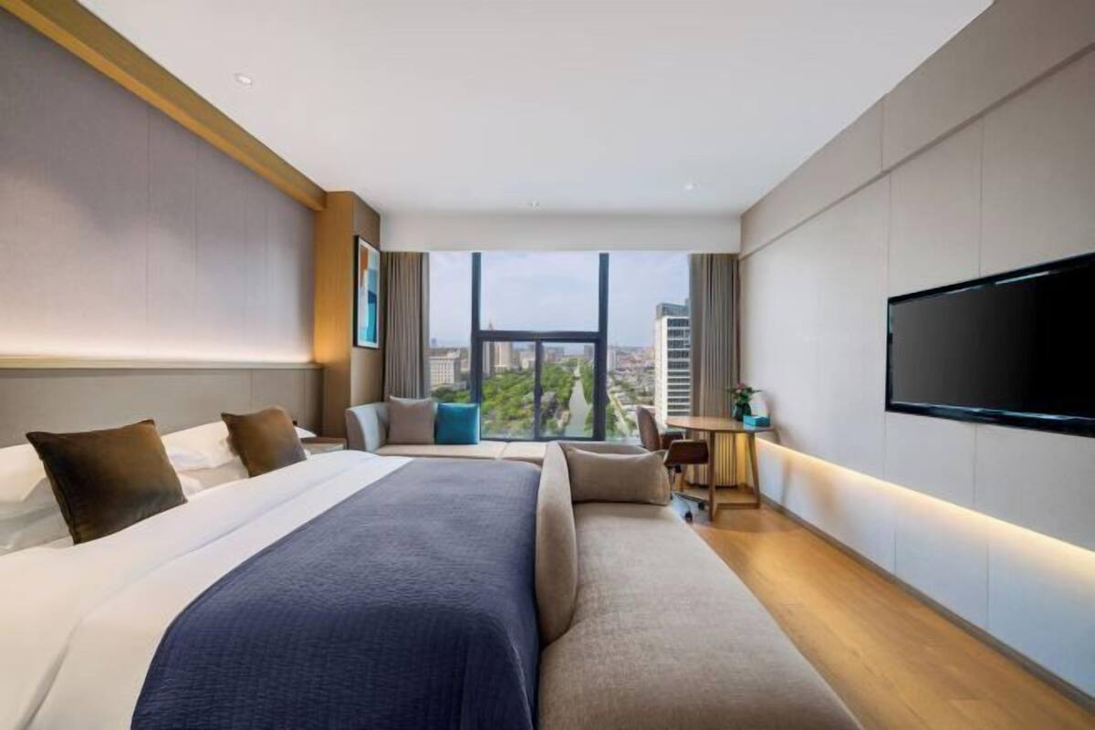 A modern hotel room with a large bed, a seating area, a TV, and a city view.