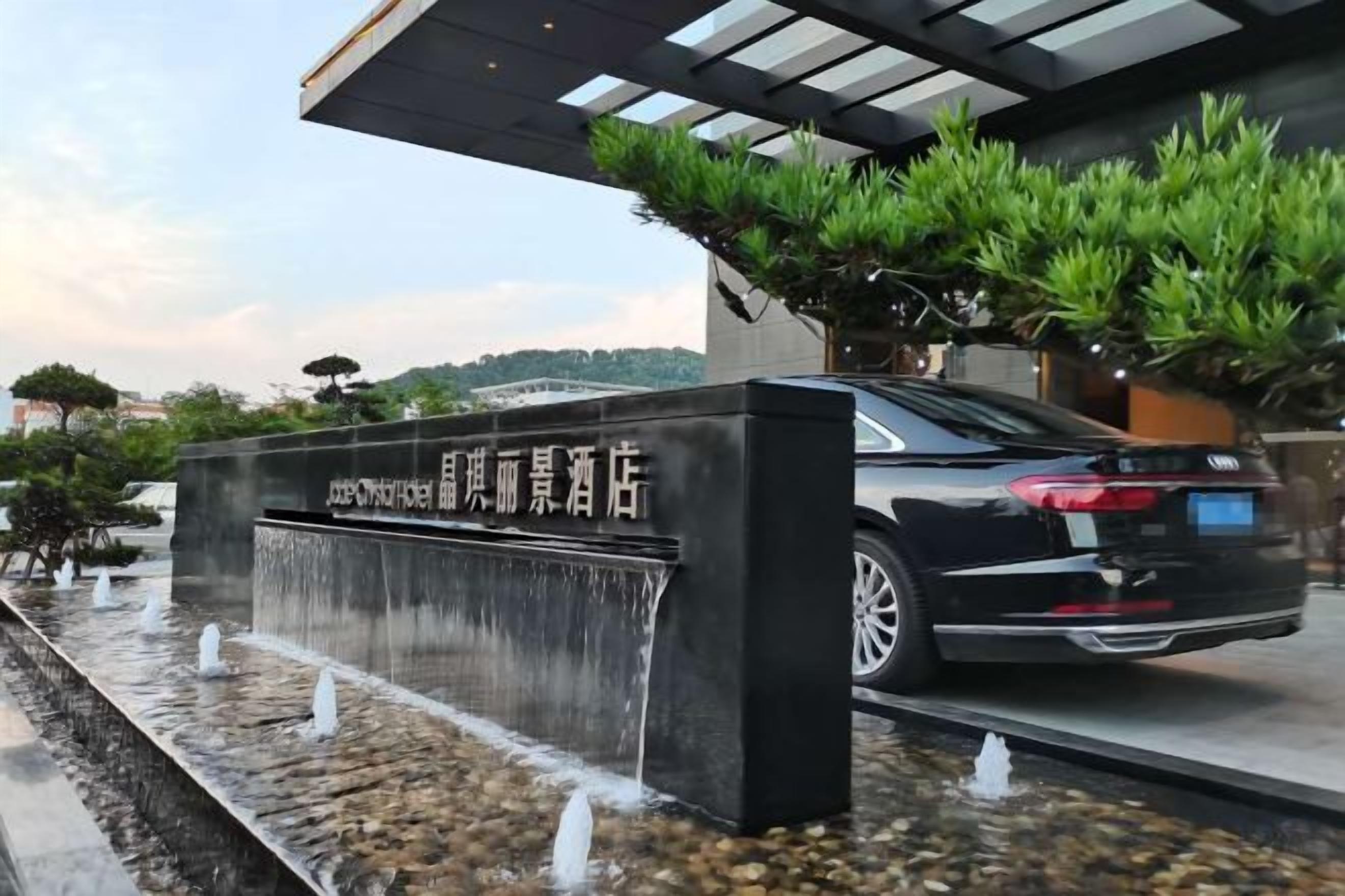 Une voiture noire est garée devant un bâtiment agrémenté d’un élément décoratif aquatique et d’une enseigne.