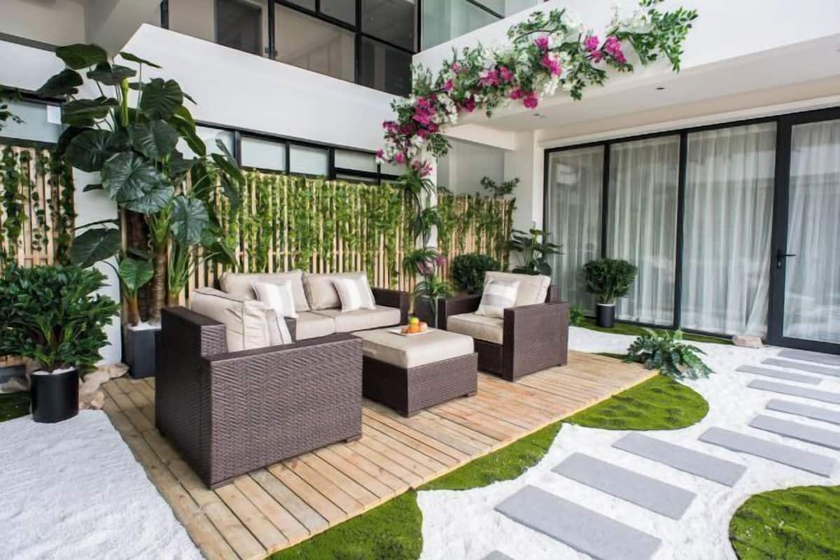 A modern outdoor living area with wicker furniture, a wooden deck, and a variety of potted plants.