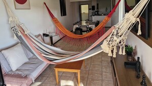 Een kamer met een hangmat, een bank, een eettafel en een keuken op de achtergrond.