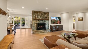A modern living room with a stone fireplace, a flat-screen TV, leather sofas, and a dining area with a wooden table and chairs.