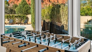 A foosball table in a room with large windows overlooking a mountainous landscape and a pool area.