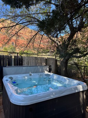 Un bain à remous installé à l’extérieur, avec une clôture en bois et des arbres en arrière-plan.