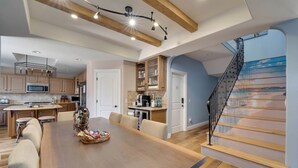 Une cuisine spacieuse avec des poutres apparentes, un coin repas doté d’une grande table et un escalier avec une rampe peinte.