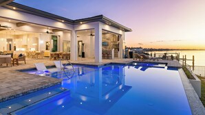Un espace piscine moderne avec vue sur l’eau, un patio couvert avec des sièges et un espace intérieur bien éclairé.