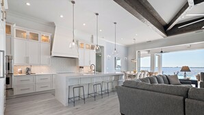 Une cuisine moderne avec des meubles blancs, un grand îlot central doté de tabourets et un éclairage suspendu.