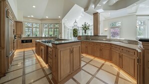 A spacious kitchen with wooden cabinets, a large island, and a view of the outdoors through large windows. - Luxurious Riverfront, Indoor Golf, Gym, Nature paradise (Kaukauna)