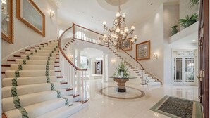 A grand staircase with a chandelier, framed artwork, and a central floral arrangement. - Luxurious Riverfront, Indoor Golf, Gym, Nature paradise (Kaukauna)