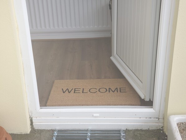 A door with a 'WELCOME' mat and a clear view into a room with wooden flooring.