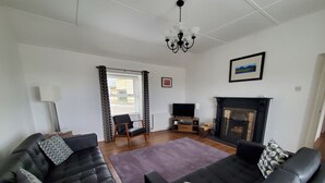 A living room with two black leather sofas, a flat-screen TV, a fireplace, and a chandelier. - The Cottage at The Burren Tyrella - your coastal base for the Mourne country. (Downpatrick)