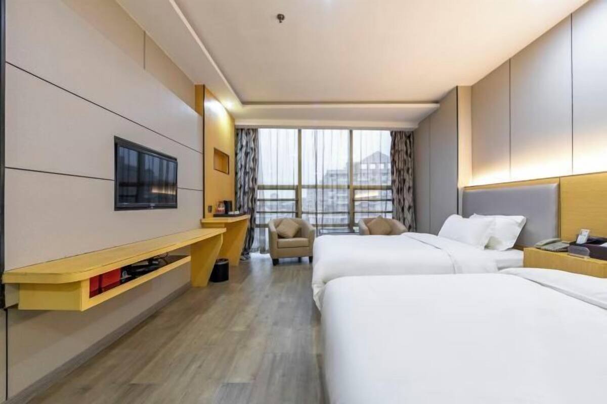 A modern hotel room with two beds, a TV, a desk, and a chair.