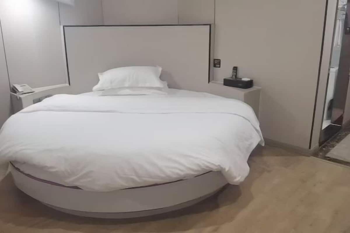 A round bed with white bedding, a bedside table with a phone, and a small object on the table.