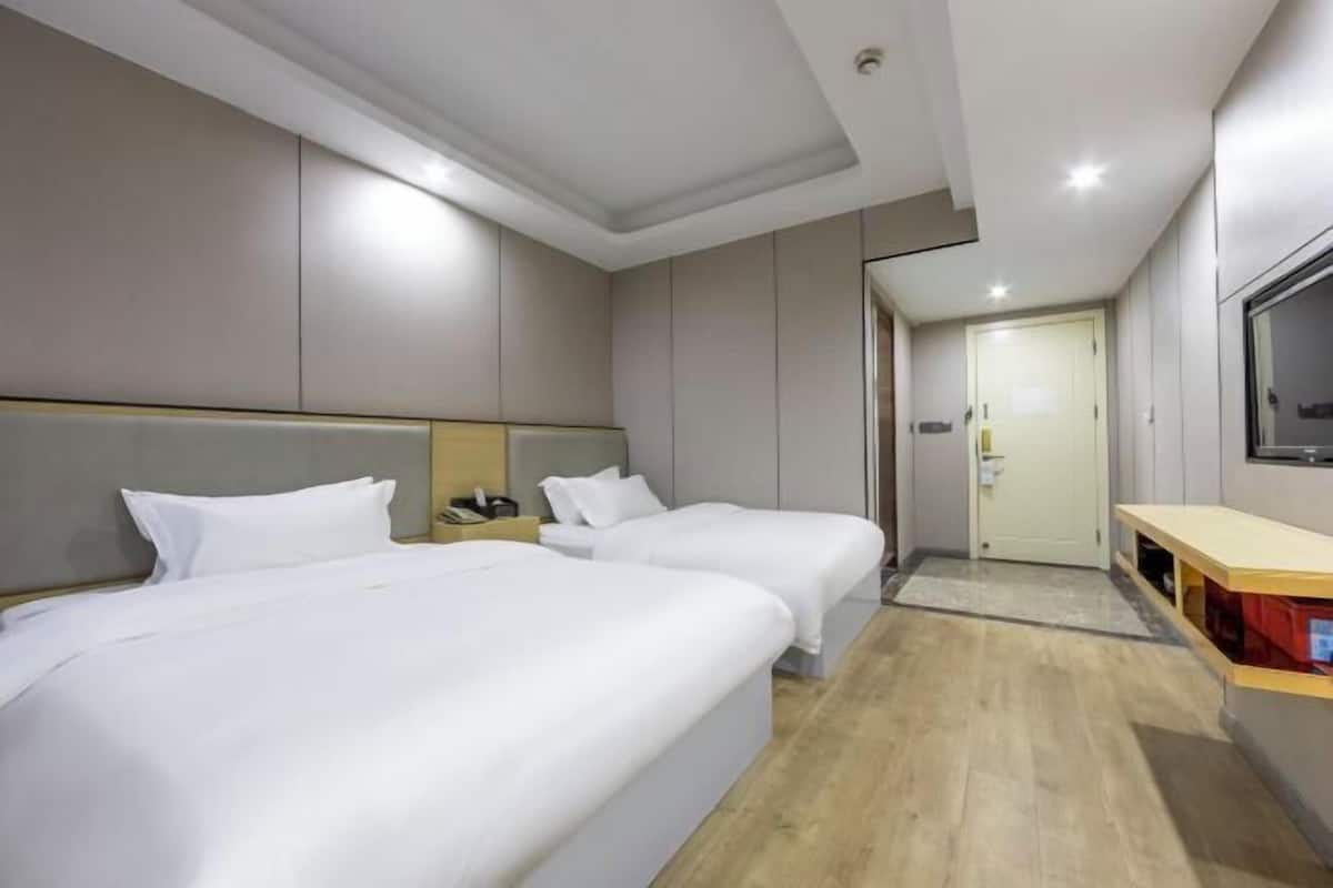 A hotel room with two beds, a TV, a desk, and a door leading to a hallway.