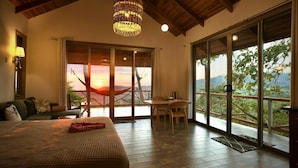 Ein Schlafzimmer mit einem großen Bett, einer Essecke und einem Balkon mit Sonnenuntergangsblick.
