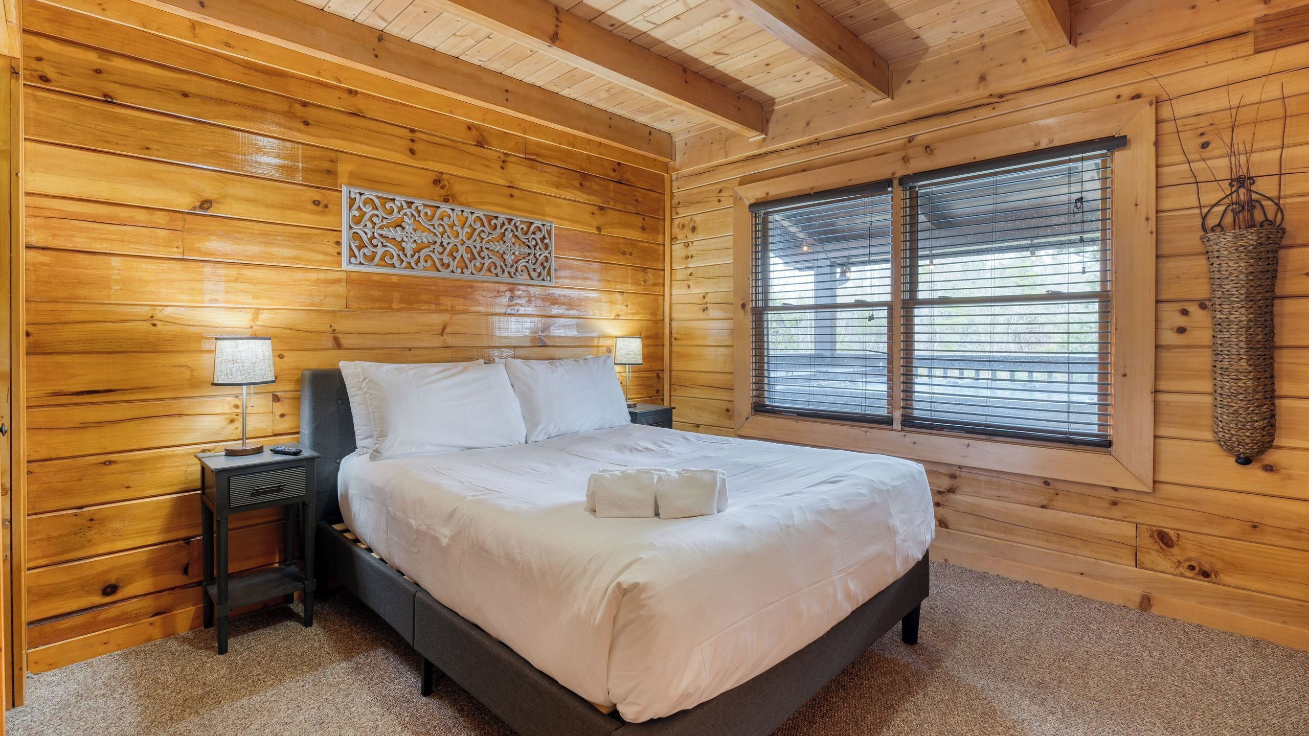 Ein Zimmer mit Holzwänden, einem Bett, Nachttischen, einer Wanddekoration und einem Fenster mit Jalousien.