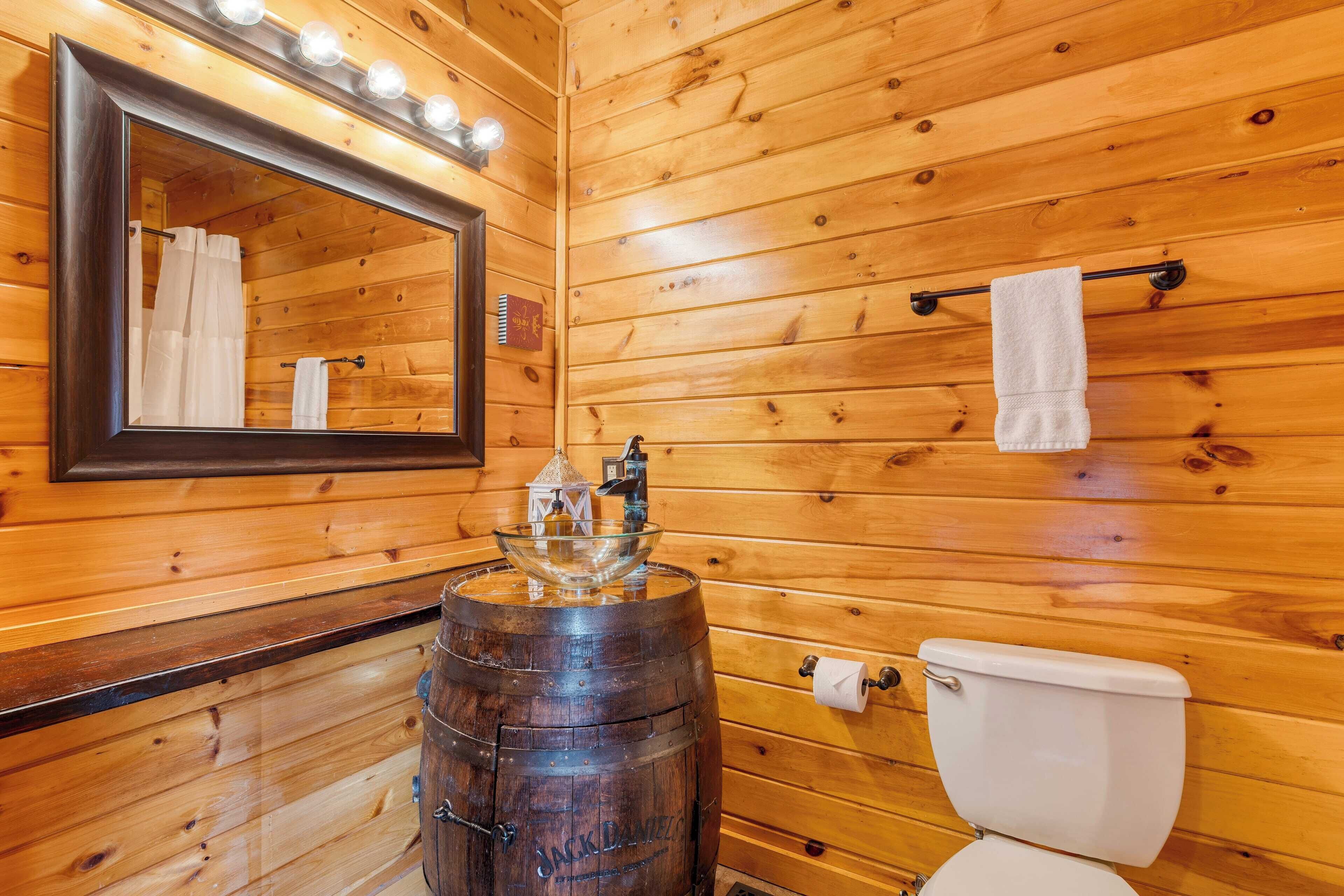 Baño de cabaña de madera con un espejo grande, un lavamanos en forma de barril de madera, un inodoro y un perchero para toallas.