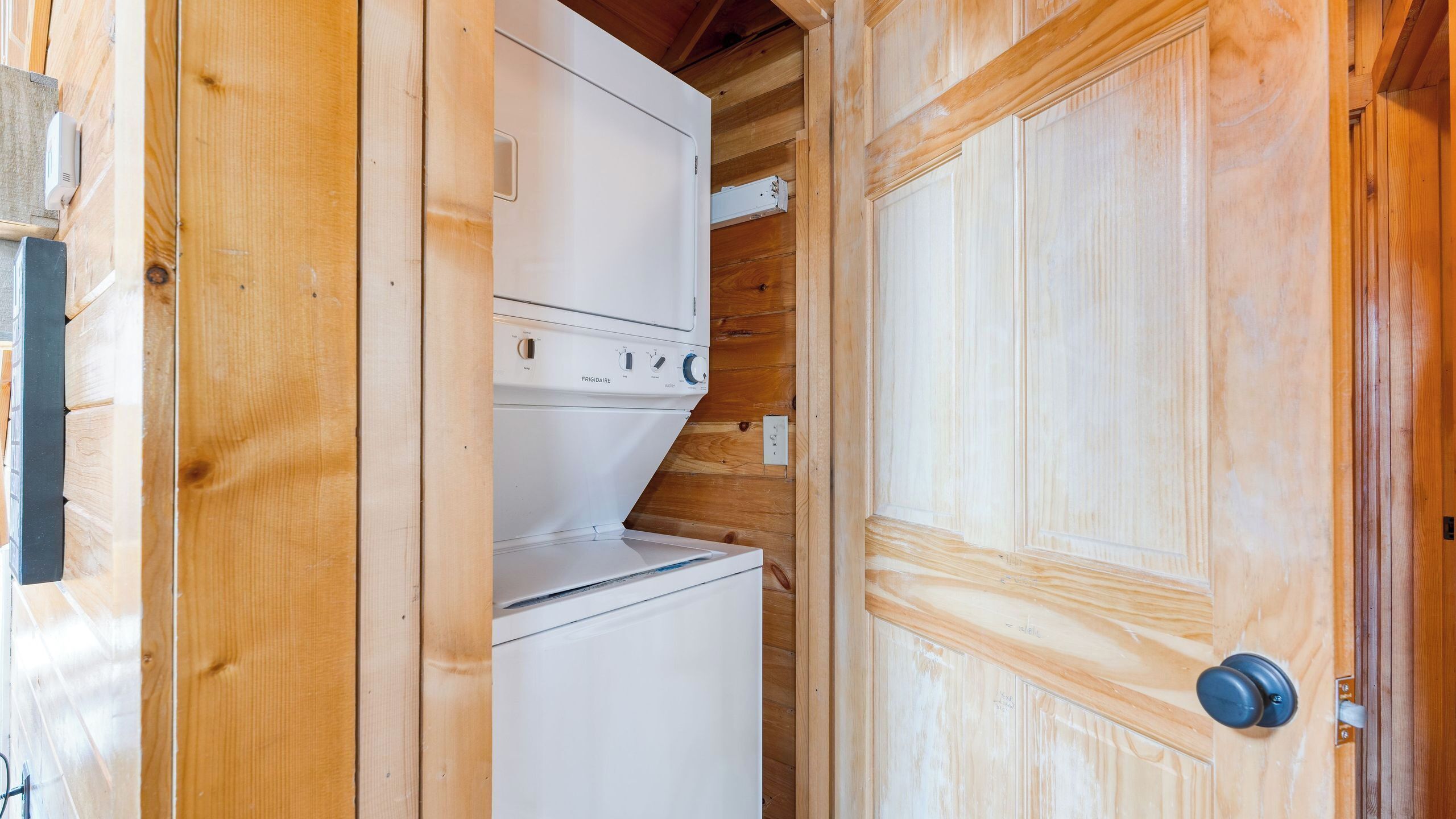 A wooden interior with a white appliance, likely a washer and dryer, and a wooden door with a round handle.