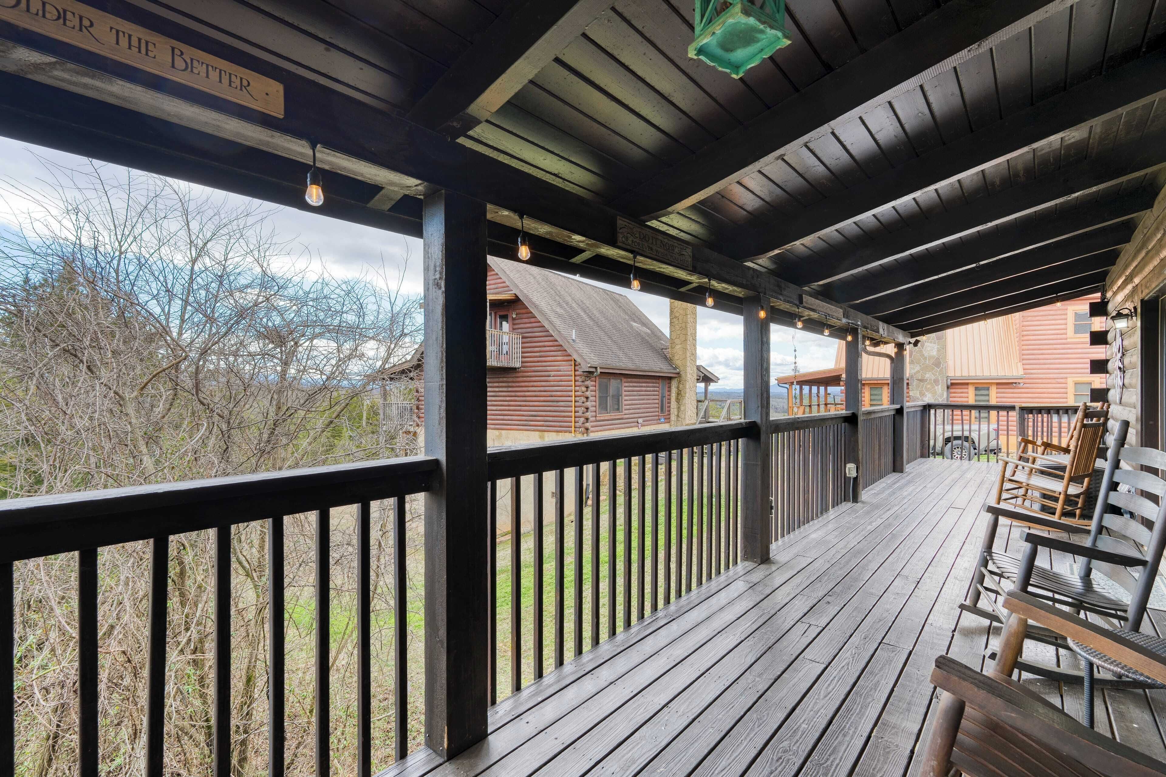 A wooden deck with a railing, benches, and hanging lights.