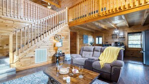 Interno di una baita in legno con una scala, un soggiorno, una sala da pranzo e una cucina.