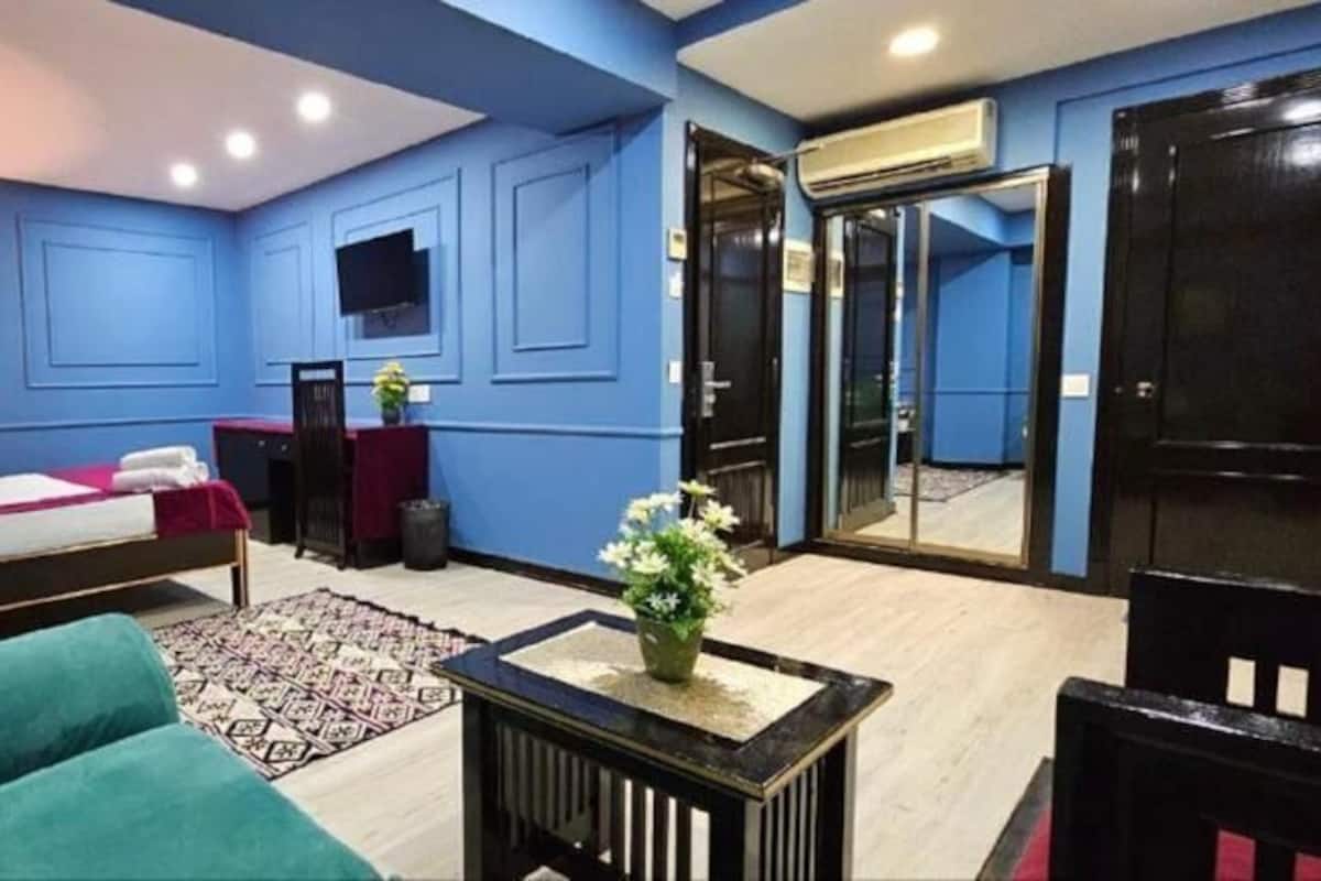 Una habitación con cama, pared azul, televisor, escritorio y puerta.