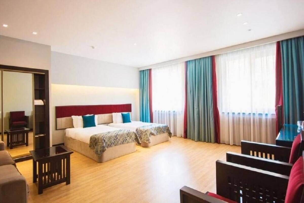 Habitación de hotel con una cama grande, un escritorio y una silla. Se ve una ventana con cortinas y un espejo en una pared.