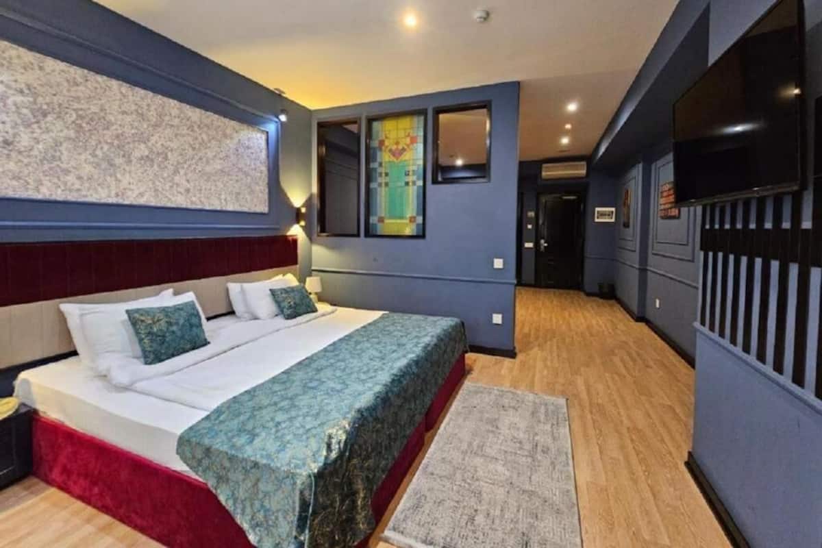 Habitación de hotel con una cama grande, una pared de acento roja, un espejo decorativo y un televisor.