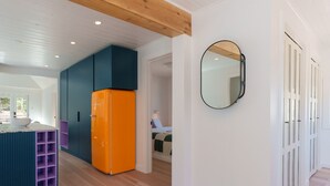 Un interior moderno con techo de madera, una cocina con un refrigerador naranja brillante y un pasillo que conduce a un dormitorio.