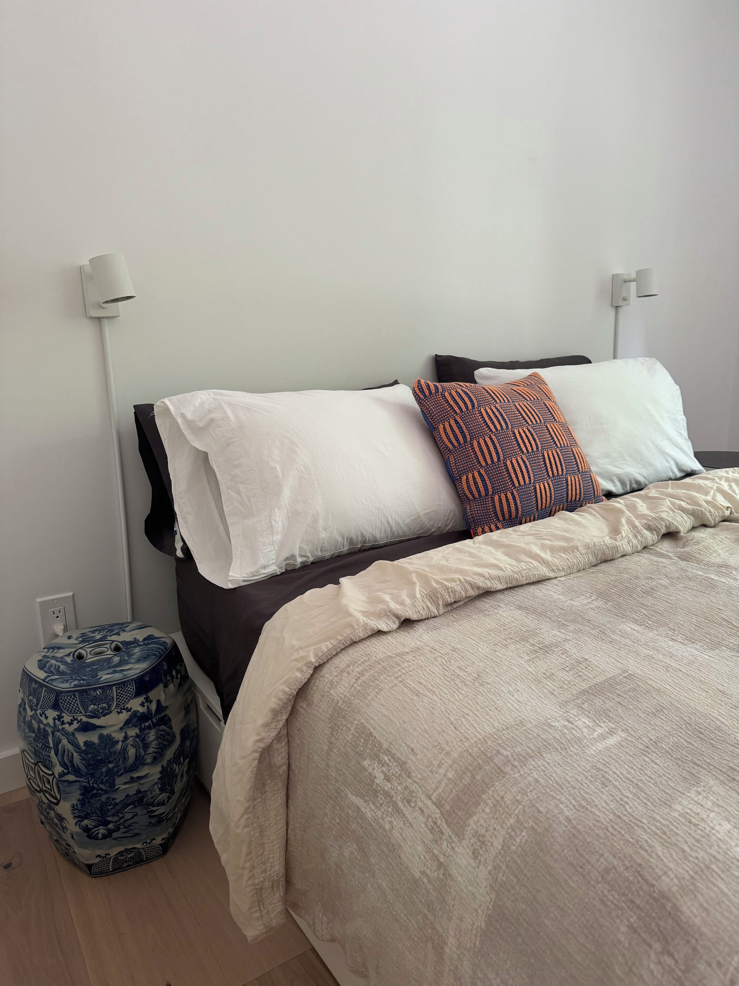 Un lit bien fait, avec une couette beige, des oreillers blancs et un plaid à motifs.