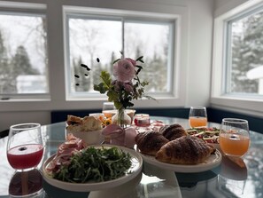 A dining table with food and drinks, a vase with flowers, and windows with a snowy view. - Charming 3-bedroom chalet with Hot Tub / BBQ /  Fireplace / AC in Flesherton (Flesherton)